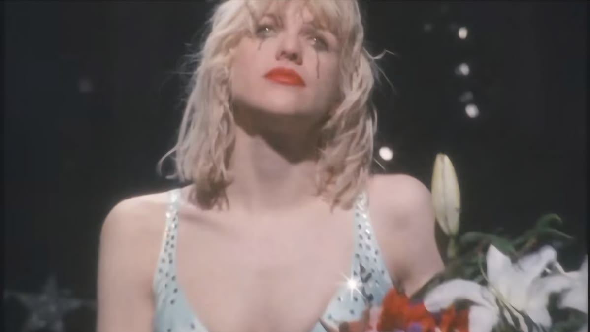 Courtney Love performing in a music video or visual shoot with smeared makeup and a crown, channeling the Carrie aesthetic